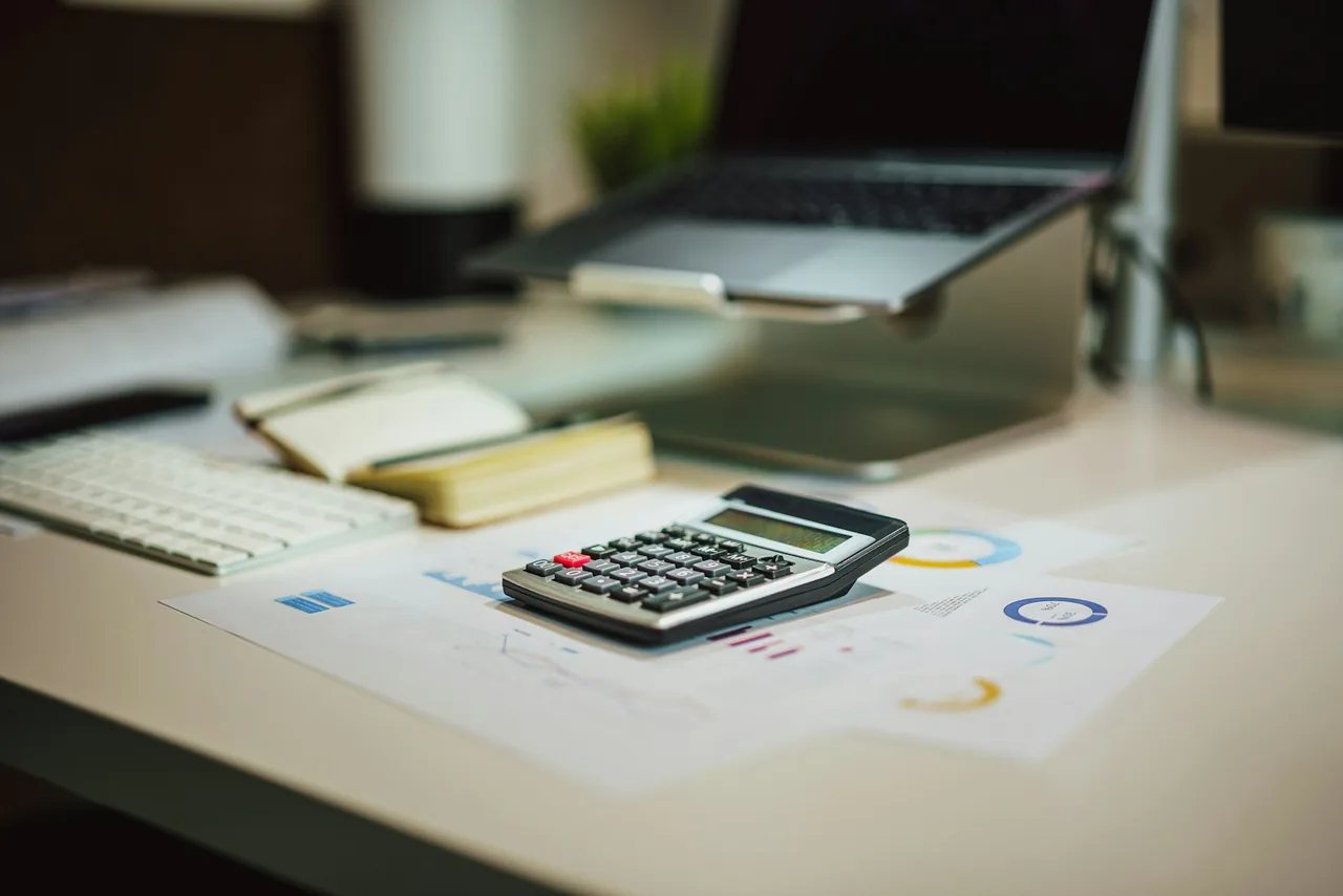 Calculatrice sur des documents de budget, à côté d’un ordinateur et d’un carnet.